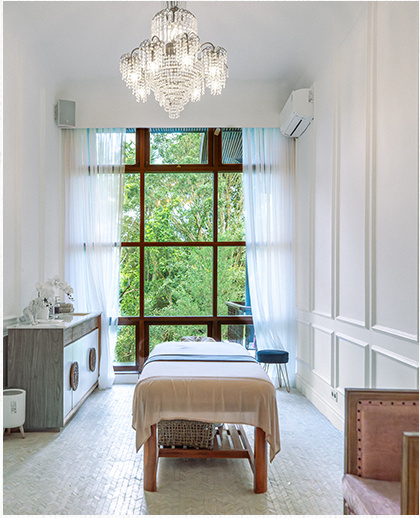 Spa treatment room with a massage bed beneath a garden-facing window.
